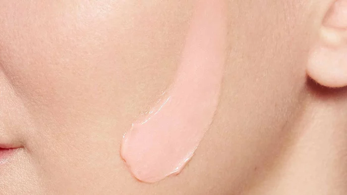 Rosa Creme wird auf eine Gesichtshaut aufgetragen, was eine Nahaufnahme des Hautpflegerituals zeigt.