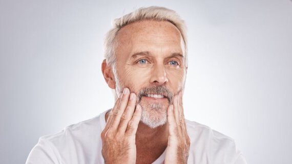 Un hombre de cabello y barba blancos se toca la cara.