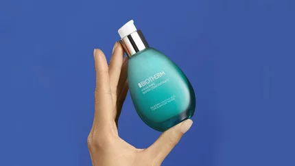 Eine Hand halt das Produkt Biotherm Aqua Pure Super Concentrate vor blauem Hintergrund.